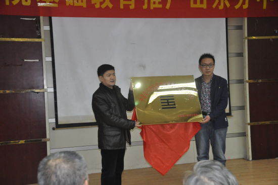 美术基础教育推广山东分中心主任、菏泽市青年美术家协会黄毅然（右）接受陈昌林先生授牌